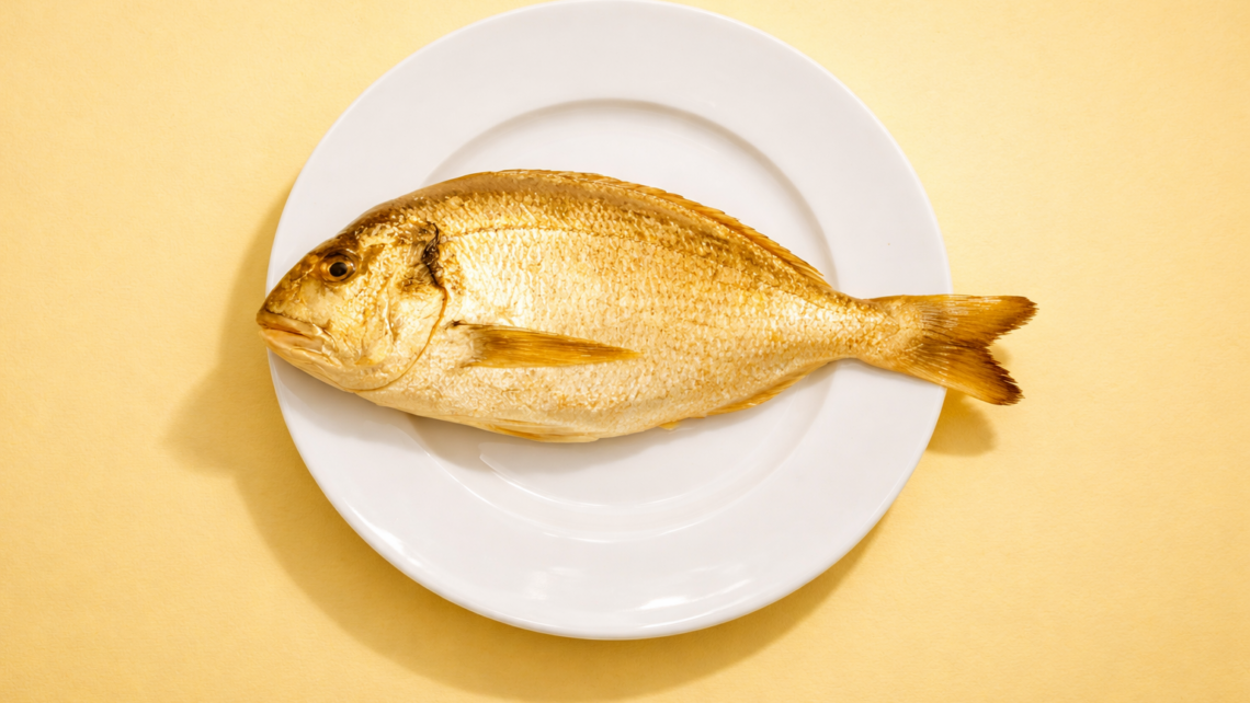 Zlatá rybka na bielom tanieri, symbolizuje zlatú baňu omega-3 mastných kyselín, žlté pozitívne ladené pozadie v pastelovej farbe